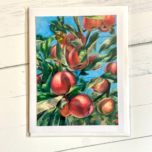 A folded white greeting card depicting my pastel painting Apples. The painting shows a close up image of an apple tree branch rich with ripe fruit. A blue sky behind emphasizes the sunlight hitting the apples.
