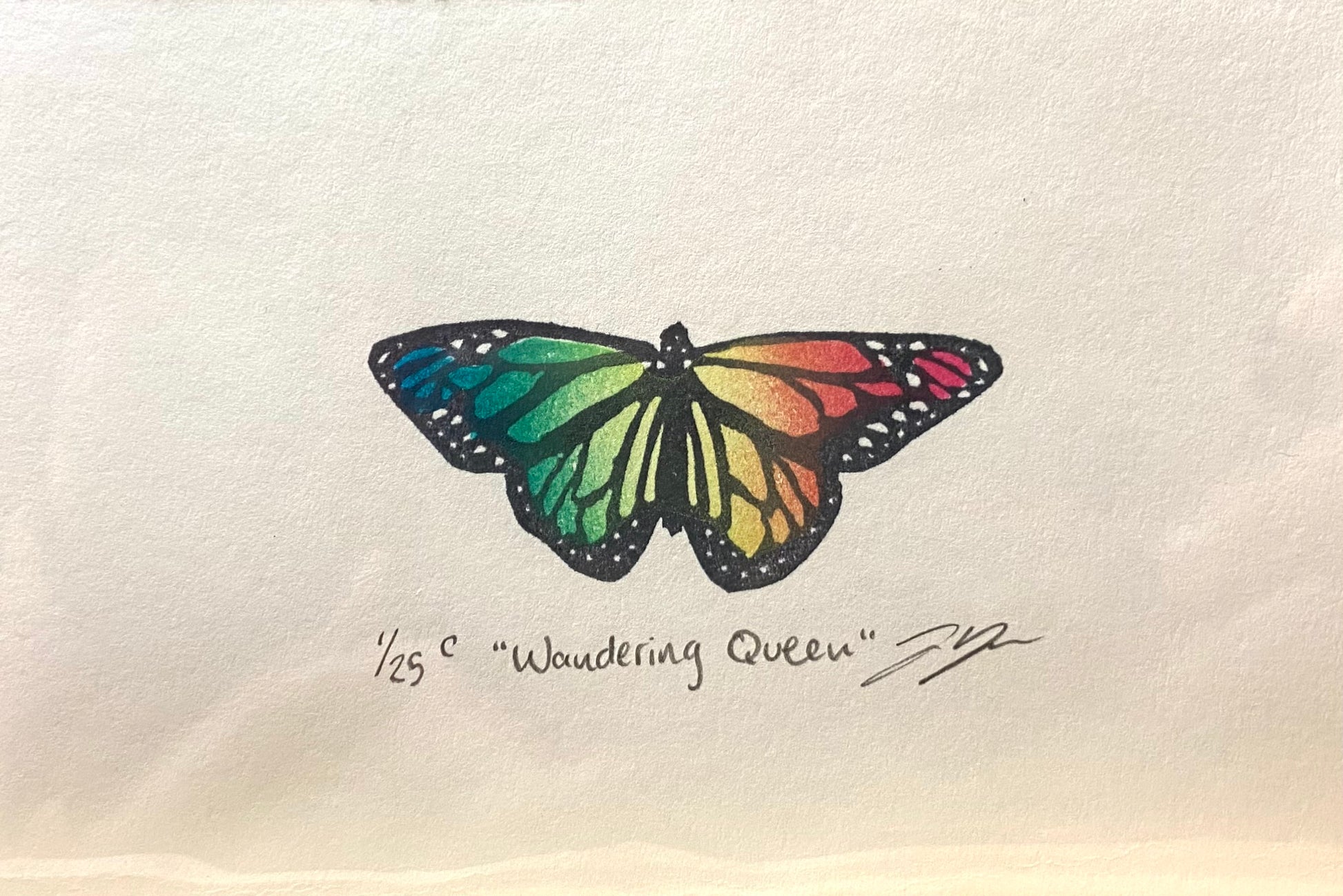 A rainbow-colored relief print of a monarch butterfly, made by hand using a carved eraser. The print is numbered, signed, and titled "Wandering Queen".