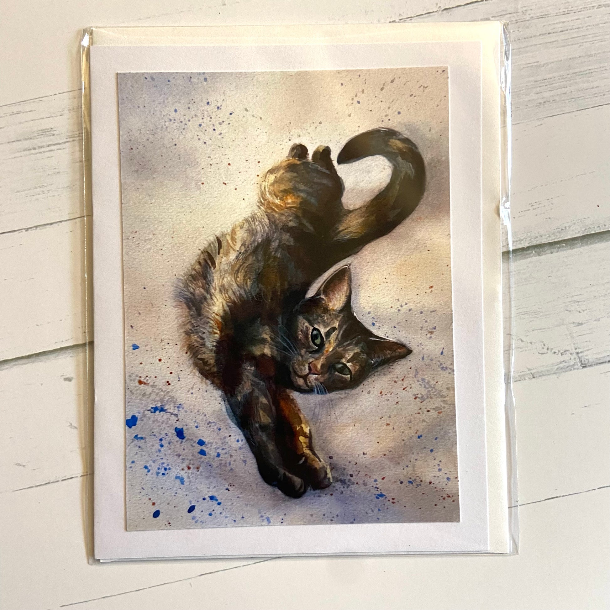 A folded white greeting card with an image of a watercolor-painted tabby cat, stretching long toward the viewer.