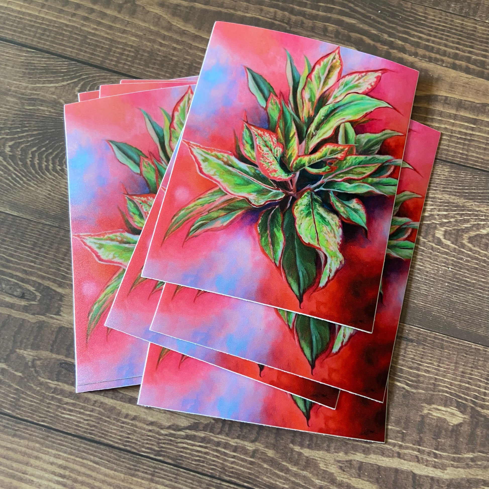A small pile of pink, rectangular stickers on a wood surface. The decals are predominantly hot pink, but with a leafy green plant growing out from center.