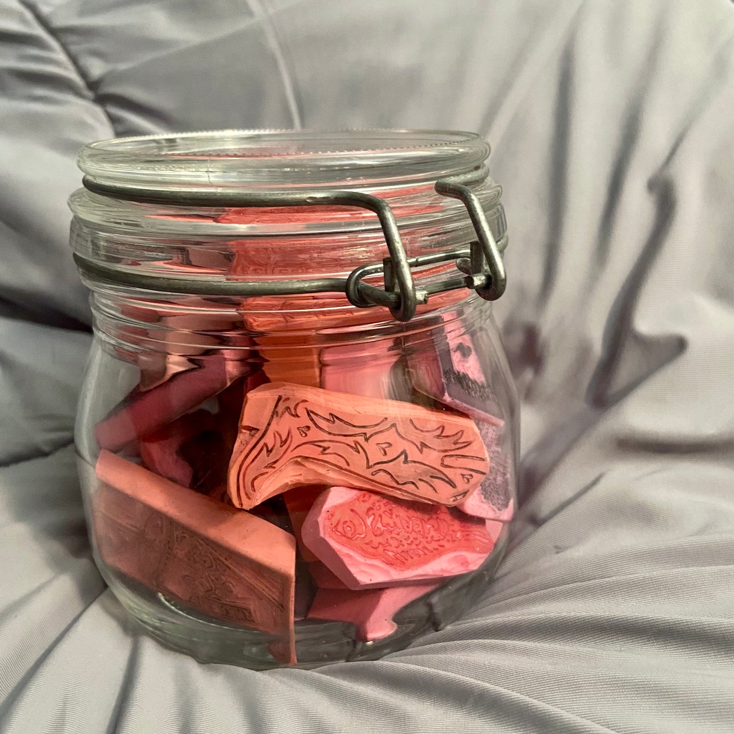 A latch-top glass jar filled with carved pink erasers. I carve the erasers by hand to make stamps or relief prints, which I then use to make art prints.