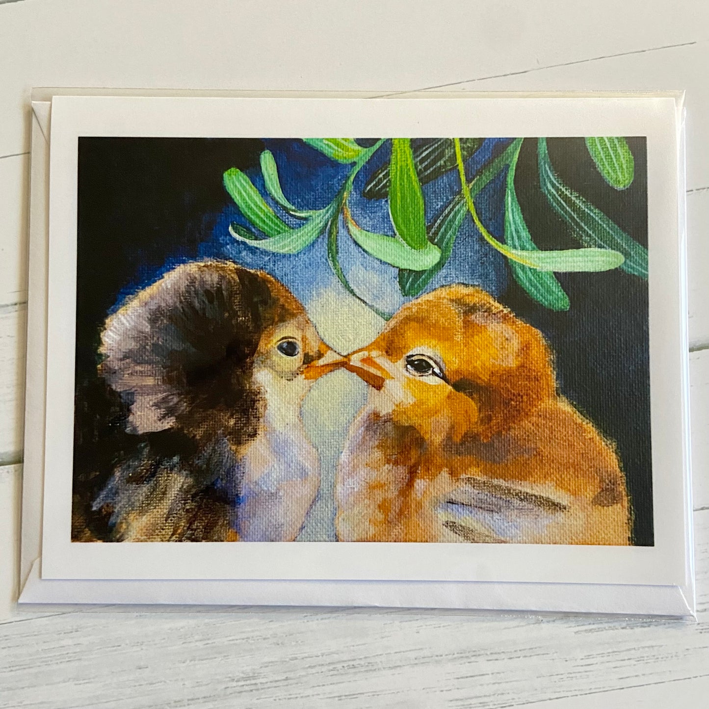 A folded white greeting card with an envelope in a plastic sleeve. The card shows a painting of two baby chicks kissing under the mistletoe.