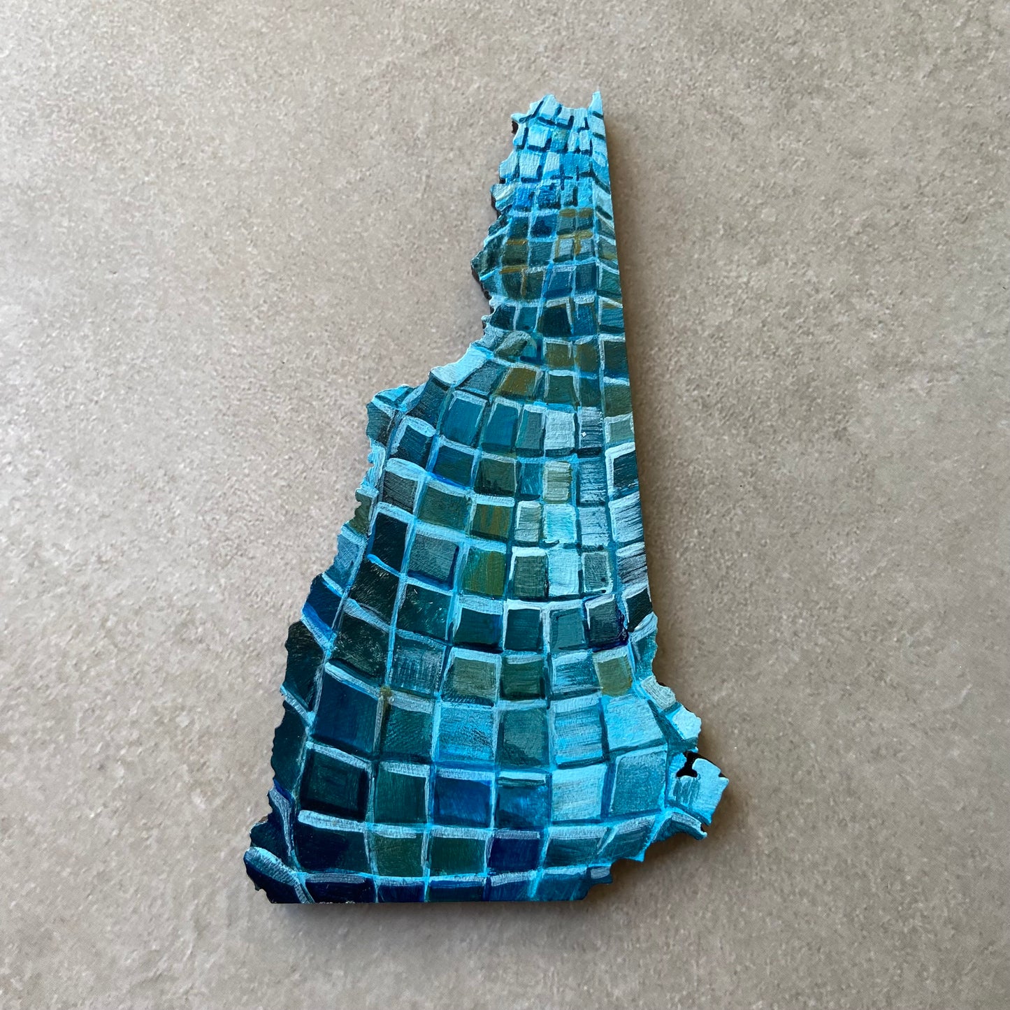 A New Hampshire- shaped painting on wood, painted with the pattern of a blue disco ball.