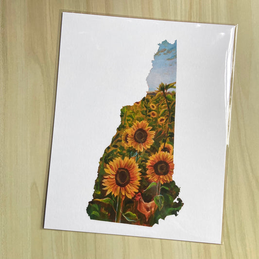 An art print on paper of a sunflower field painting in the shape of New Hampshire. Outside the map outline shape is white. The focus is three yellow sunflowers and an orange hen near the bottom. More flowers are farther behind and the sky is blue.