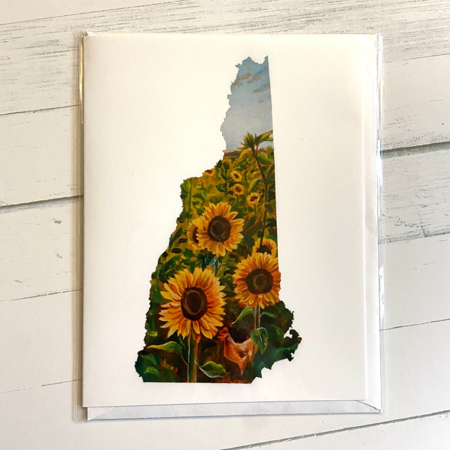 A folded white greeting card with an image of my painting New Hampshire III, depicting a sunflower field in the shape of the state of NH.