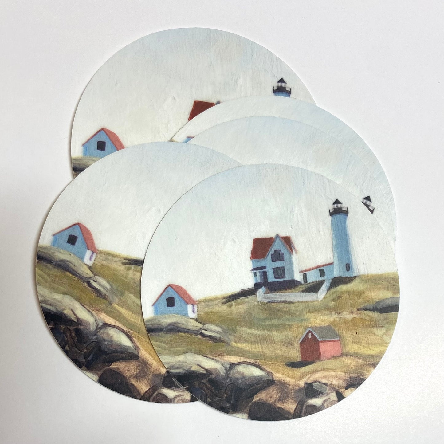 A pile of stickers of Jackie Hanson's Nubble Lighthouse painting. Nubble Light is located in York, Maine.