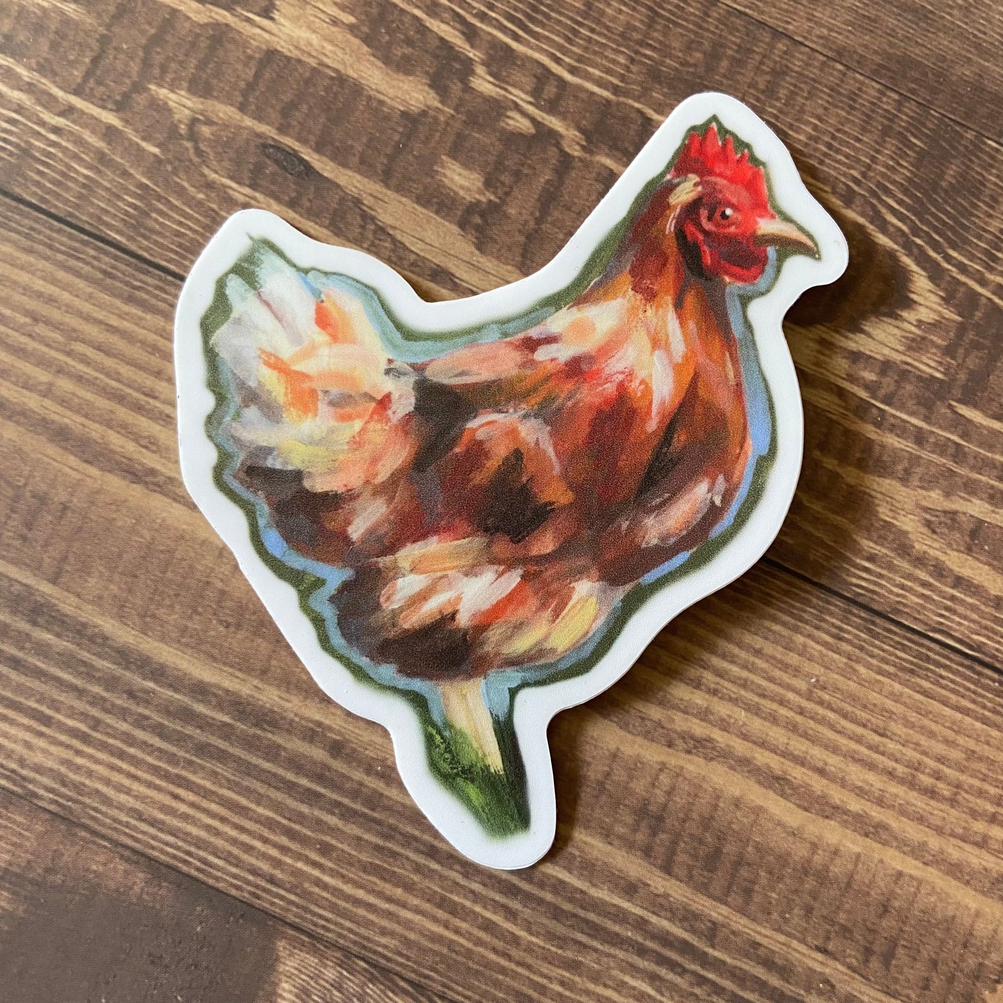 A sticker of an orange chicken viewed from the side, resting on a wooden surface. The hen is painted with gouache, with visible painterly brush strokes. Decal is die-cut to shape with a thin white border.