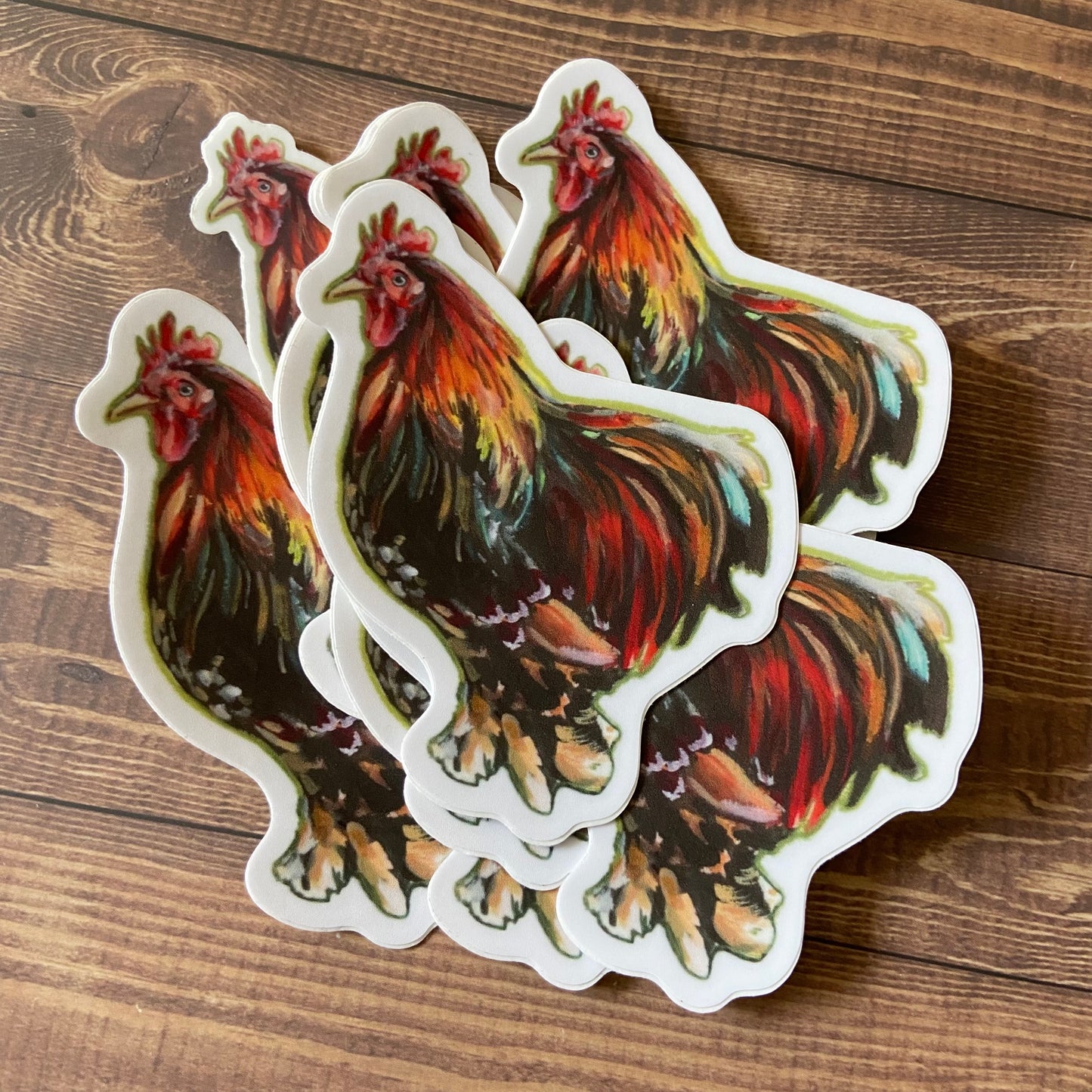 A small pile of rooster decals. Each sticker shows a painted male chicken in profile, die cut to shape with a narrow white border.