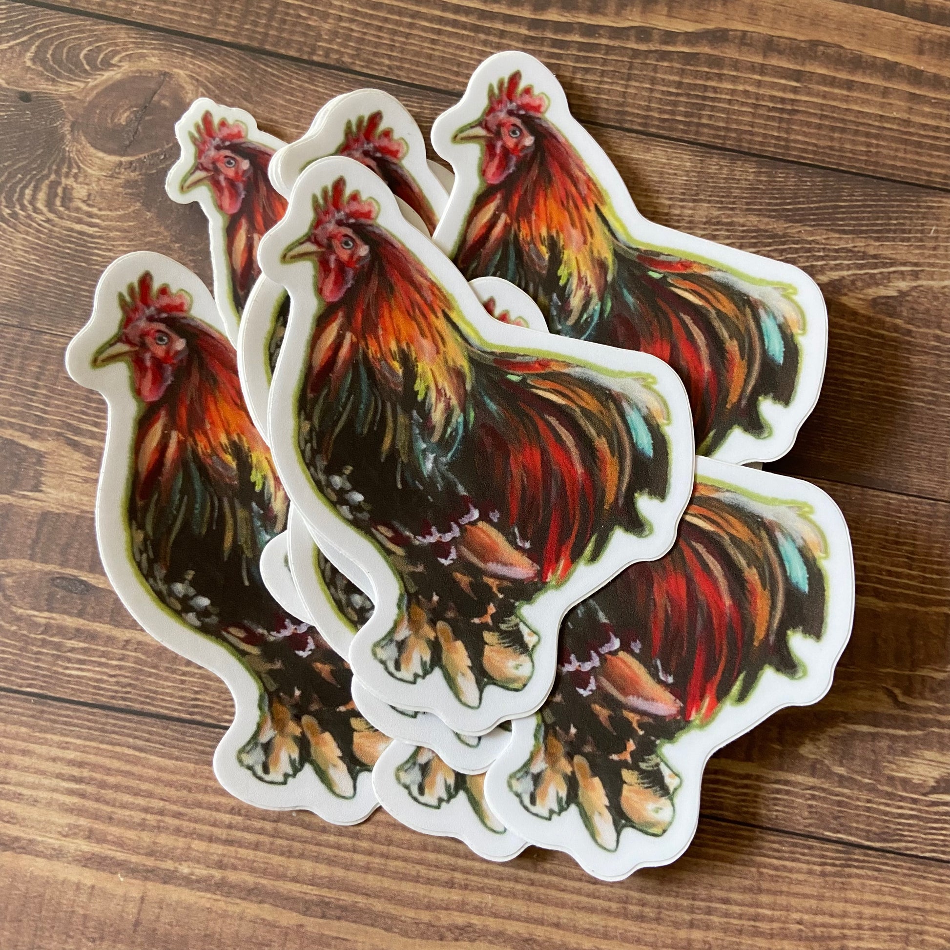 A small pile of rooster decals. Each sticker shows a painted male chicken in profile, die cut to shape with a narrow white border.