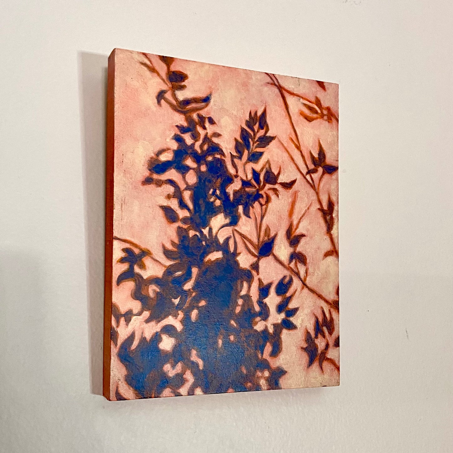 A vertical, rectangular painting of a plant's shadow. Blue shadows of leaves cover the picture plane in a natural pattern, more concentrated at the bottom and growing smaller toward the top. The negative space is pale yellow-orange.