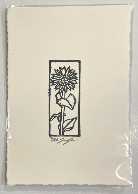 A black and white relief print of a sunflower, emphasizing outlines for form in the way of stained glass. The print is made by hand using a carved eraser and is numbered and signed.