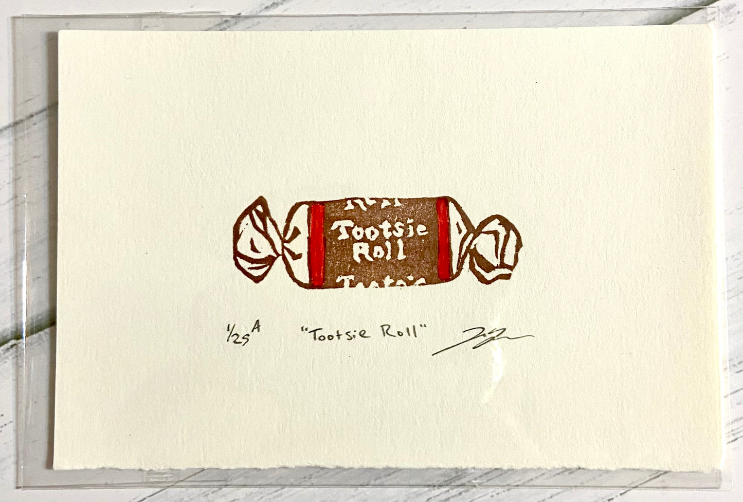 A two-color relief print of a Tootsie Roll candy. The prints are made by hand from a carved eraser and are numbered, titled and signed.