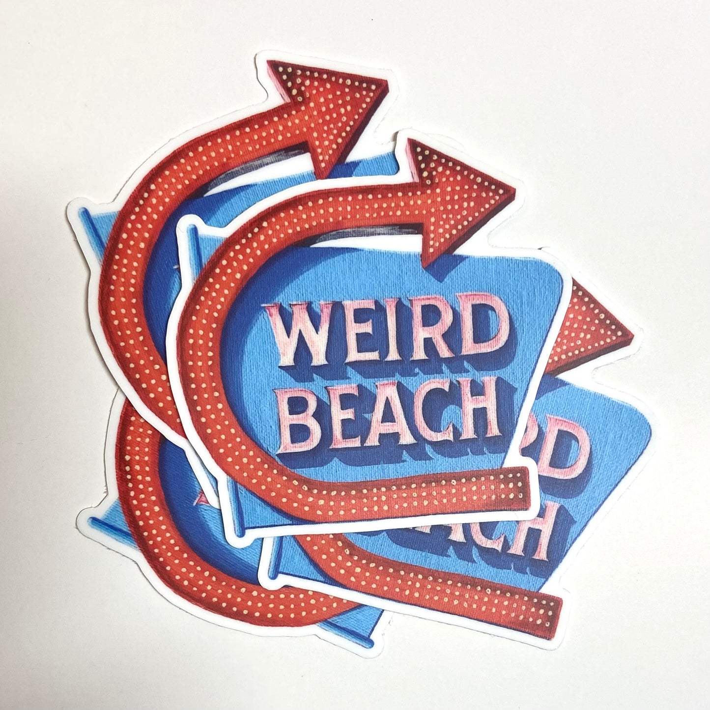 A pile of stickers of the iconic Weirs Beach sign reading WEIRD BEACH.