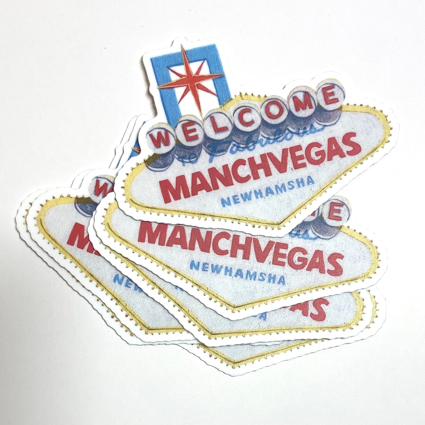 A pile of stickers showing the Las Vegas sign repainted to read "Welcome to Fabulous ManchVegas New Hamsha".