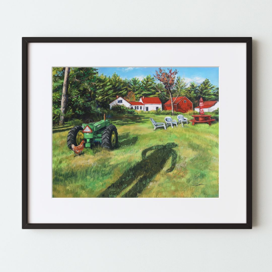 A mockup of a landscape art print in a black frame with a white mat. The artwork shows a farmhouse with a barn and tractor on a green grassy field. There is a long shadow of a man walking coming from the bottom edge of the piece.
