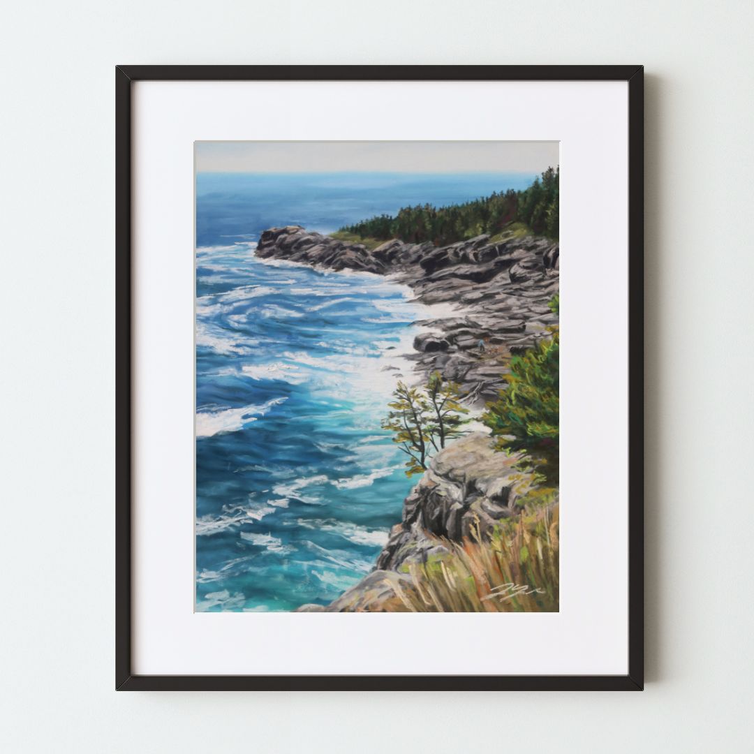 A mockup of a landscape art print in a black frame with a white mat. The painting shows a rocky cliff and further beach, both with green forest on the land and bright blue ocean beside. Closer is a small pine growing from the cliff and dry brush.