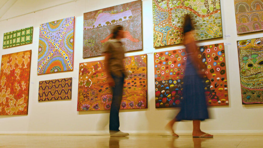 A stock image of two people walking by a wall of abstract paintings.