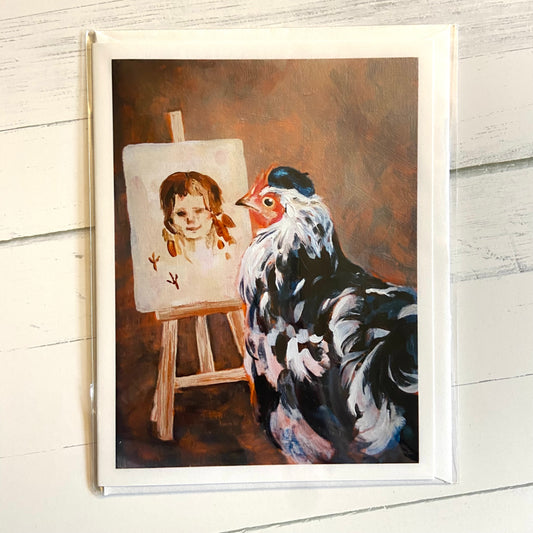 A folded white greeting card with an image of my acrylic painting, Artist Hen. A black and white, beret-clad hen stands before an easel with a simple painting of a human woman's face. The painting is signed with two bird footprints.