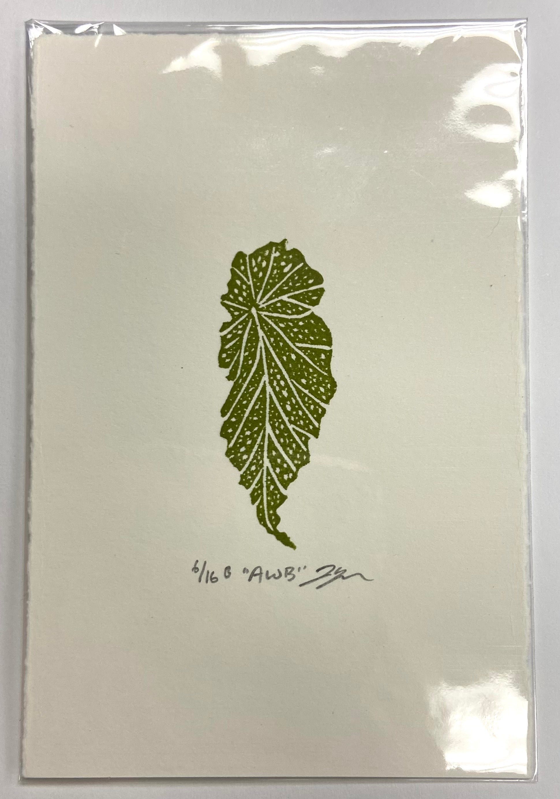 An olive green relief print of a spotted angel-wing begonia leaf. The prints are made by hand with carved erasers and are signed, numbered, and titled. 