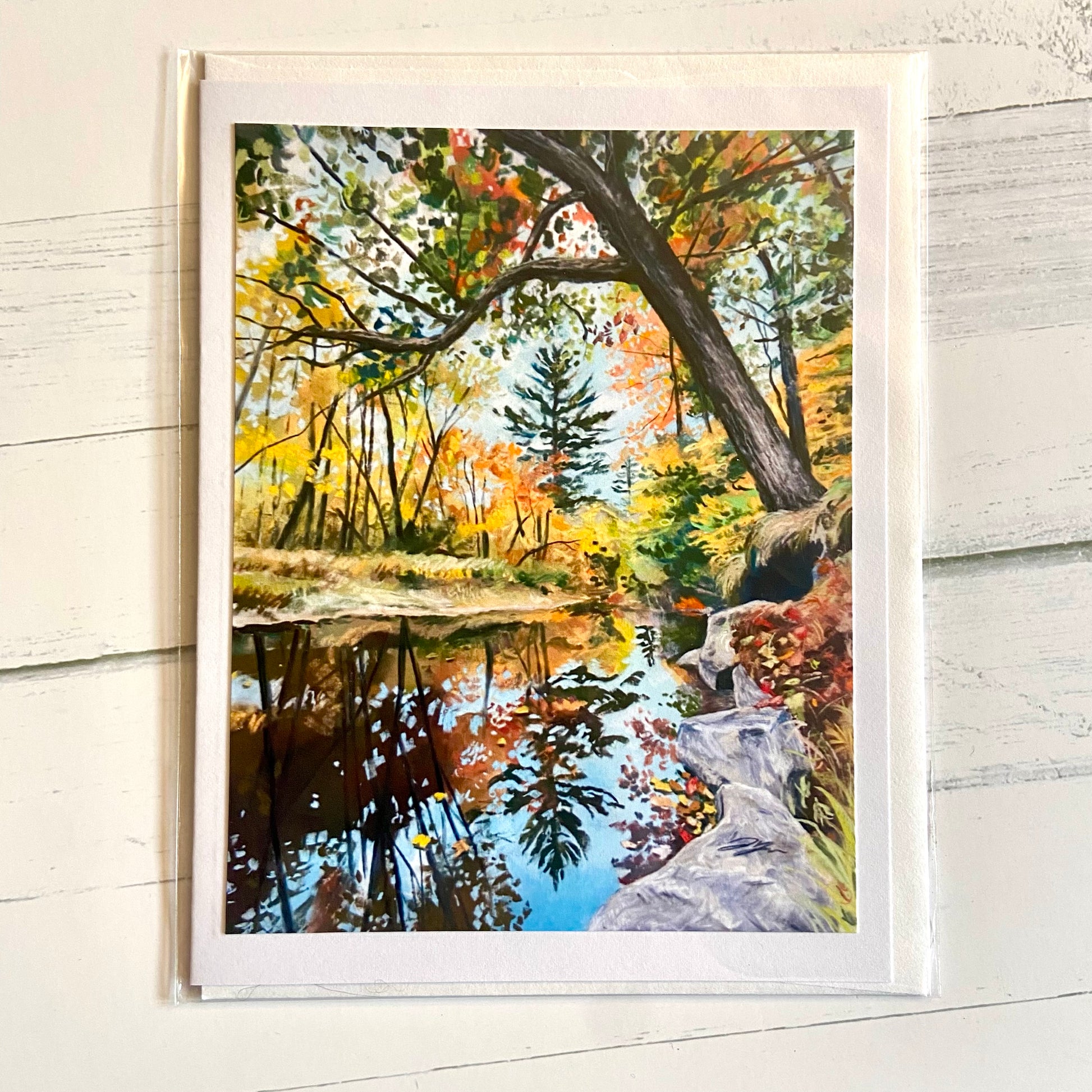 A folded white greeting card with an image of my soft pastel landscape painting, Blackwater. Shown is the mirrorlike Blackwater River of rural New Hampshire, with fall colors in the surrounding trees and one tree in the foreground leaning gracefully over the water.