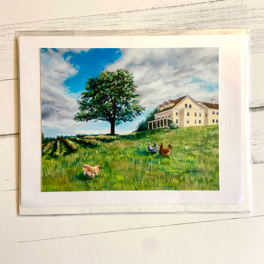 A folded landscape-style greeting card with a painted image of a hill with a majestic tree and yellow farmhouse at the top. There are chickens, a field of crops and a blue sky. 