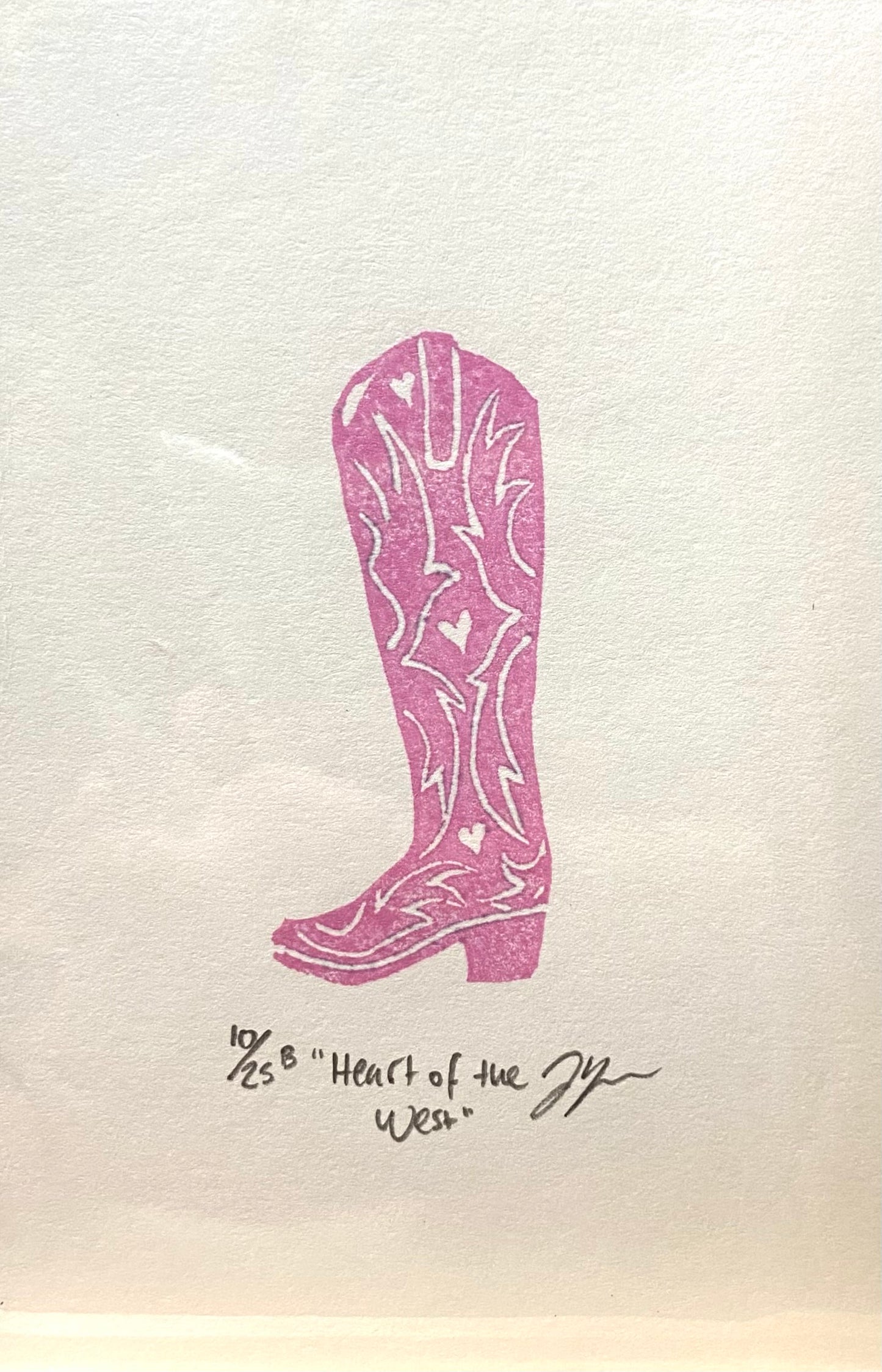 A pink and white relief print of a cowgirl boot, made by hand using a carved eraser. The print is numbered, signed, and titled "Heart of the West".