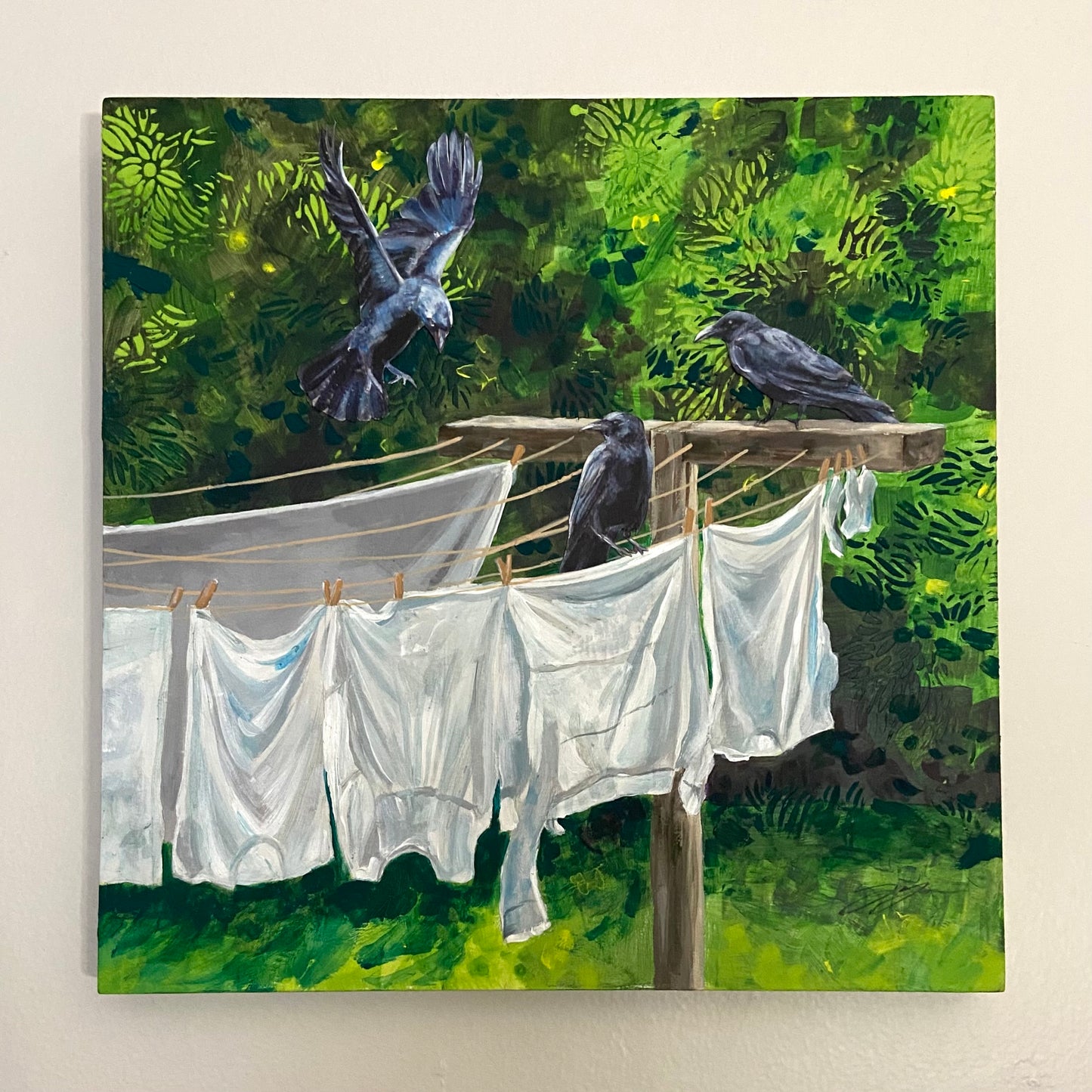 A painting of three crows hanging out at a clothesline drying white laundry. The crows are collaged-on paper. The background is green and abstract, suggesting foliage. 