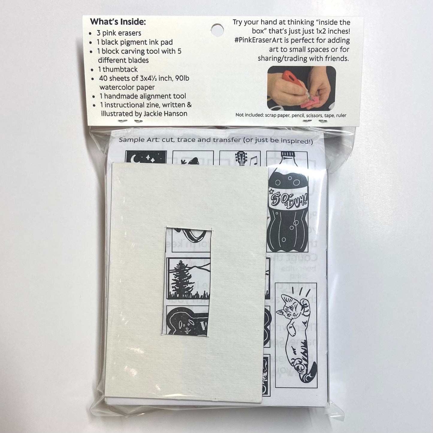 The backside of a packaged eraser art printmaking kit on a white background. A list of contents is visible, listing 3 pink erasers, 1 black pigment ink pad, 1 block carving tool with 5 different blades, 1 thumbtack, 40 sheets of 3x4.5 inch 90lb watercolor paper, 1 handmade alignment tool, and 1 instructional zine written and illustrated by Jackie Hanson.