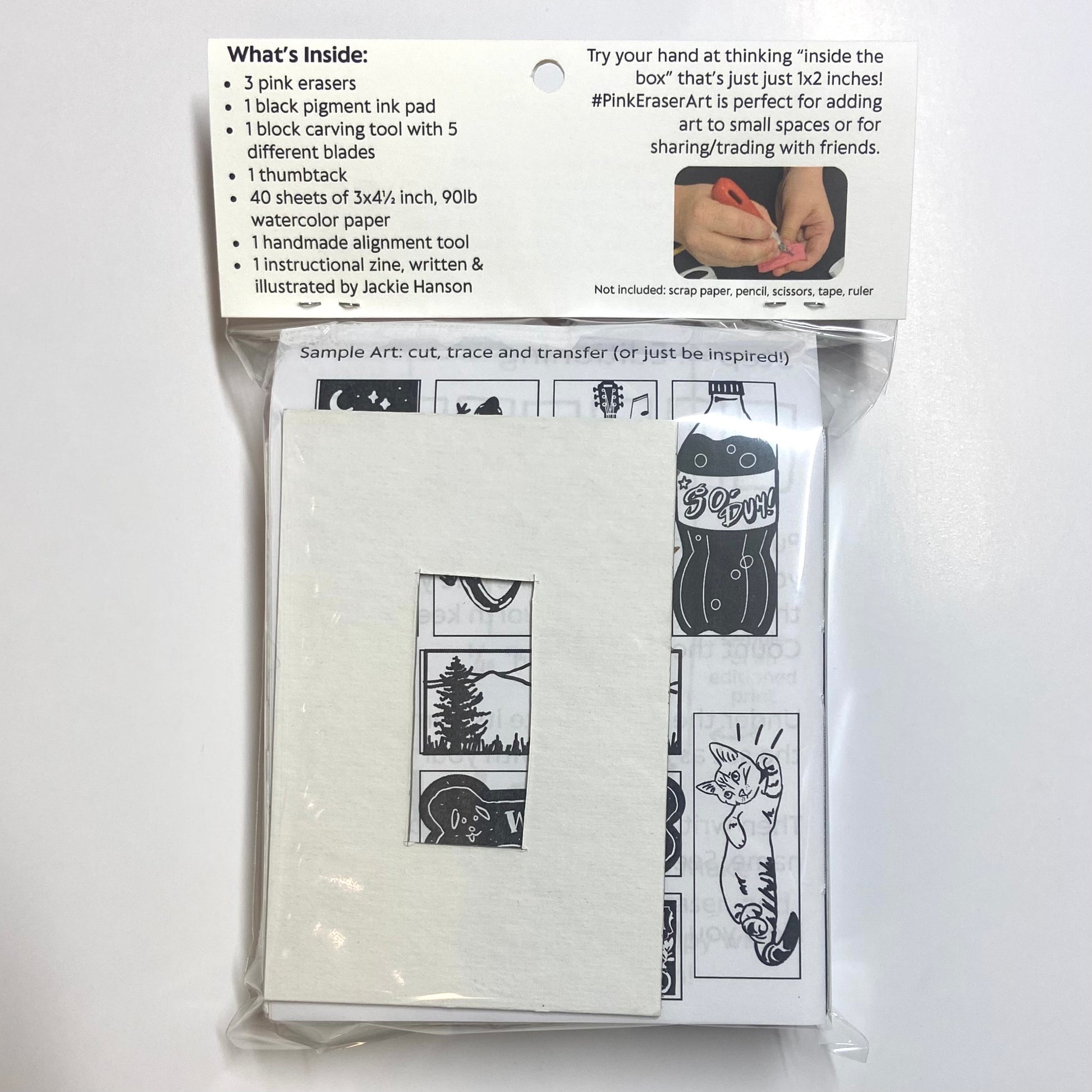 The backside of a packaged eraser art printmaking kit on a white background. A list of contents is visible, listing 3 pink erasers, 1 black pigment ink pad, 1 block carving tool with 5 different blades, 1 thumbtack, 40 sheets of 3x4.5 inch 90lb watercolor paper, 1 handmade alignment tool, and 1 instructional zine written and illustrated by Jackie Hanson.