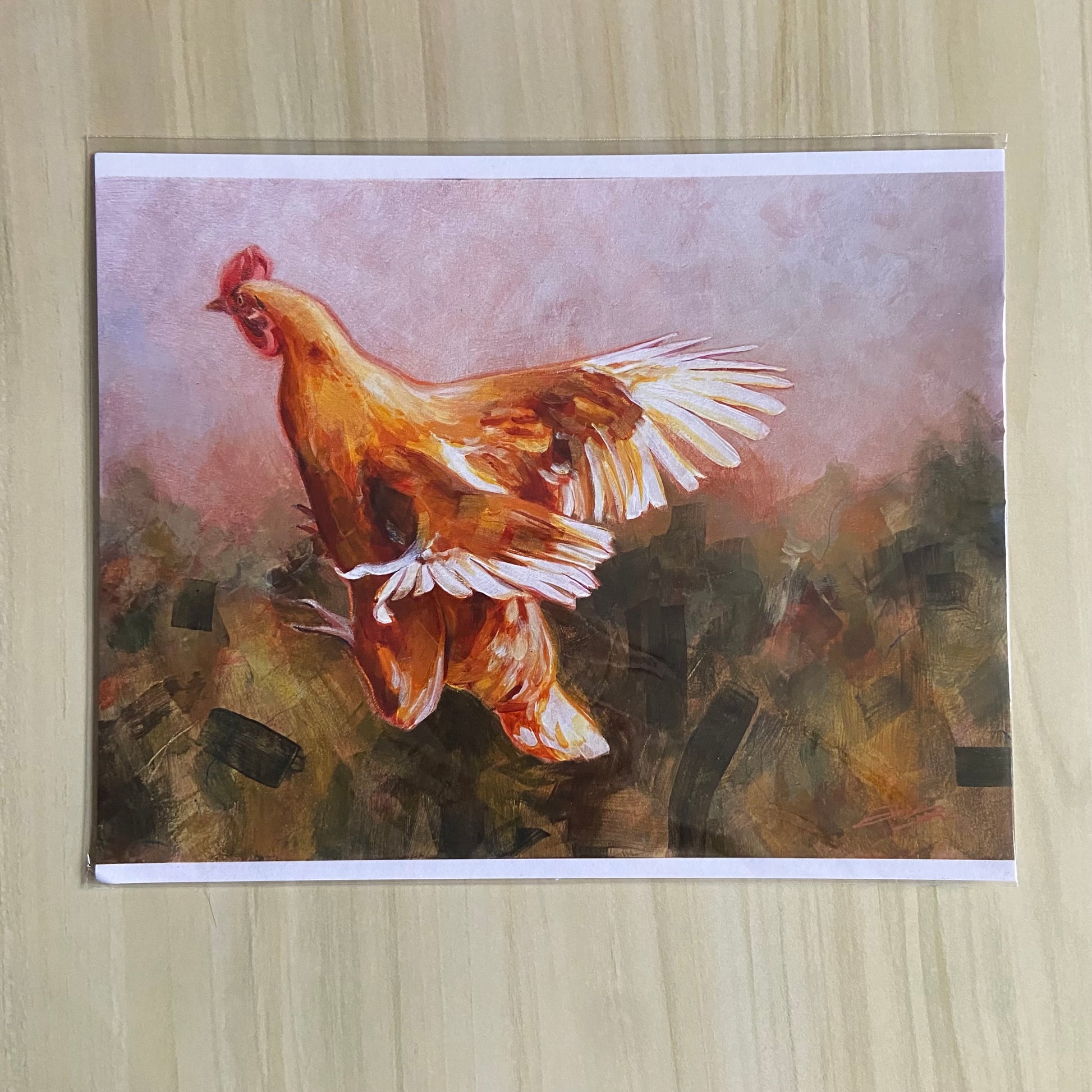 An art print of an orange chicken in flight over an abstract background. The print has thin white borders at top and bottom and is sealed in a clear plastic sleeve.