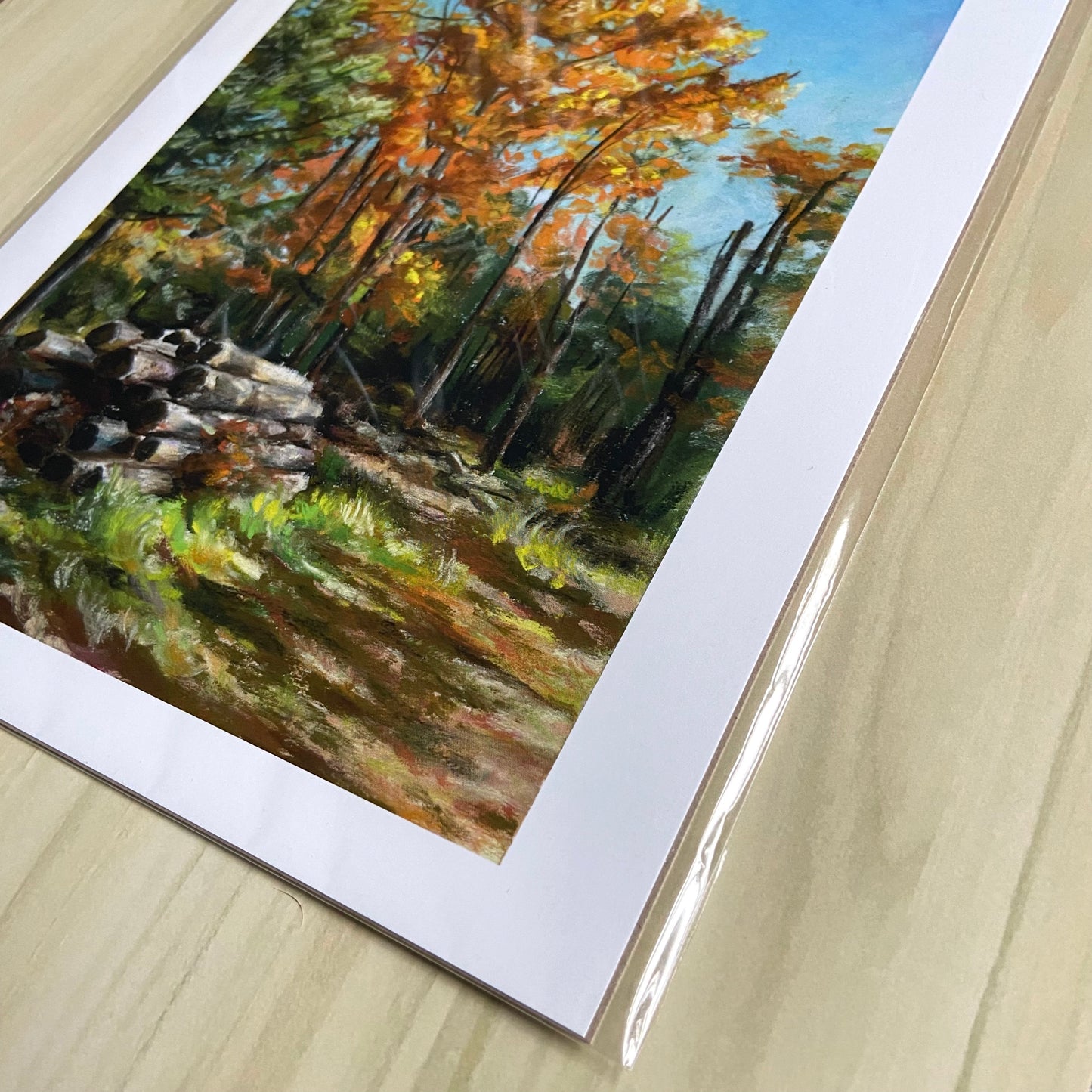 A detail look at the print. The grainy pastel texture from the original painting can be seen here. There is sunlight and shadows on the ground in front, spilling into the woods behind and especially in the tops of the trees in orange fall foliage.