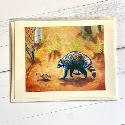 A folded cream-colored greeting card with an image of my gouache painting, Friends. The painting shows an orange forest where a raccoon and a chipmunk approach each other. 