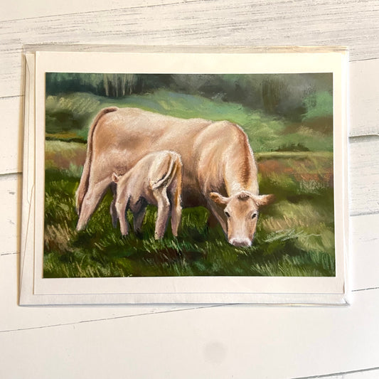 A folded greeting card with an image of a beige mother cow feeding her calf while grazing on a grassy hill. The image is painted with soft pastels, giving it a chalky texture.