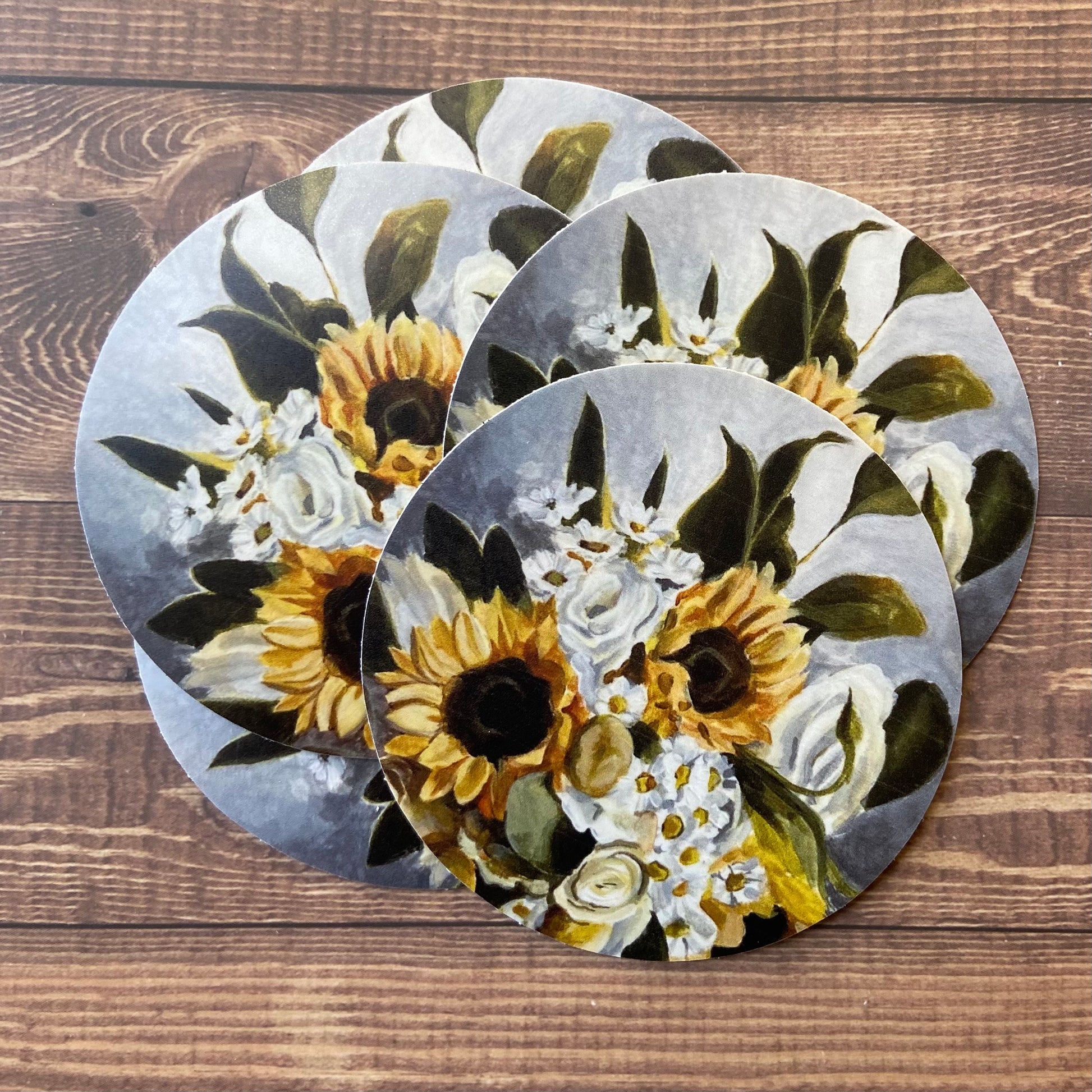 A small pile of round stickers of my painting "Green Gold", depicting a bouquet of sunflowers, daisies, white roses and greenery.