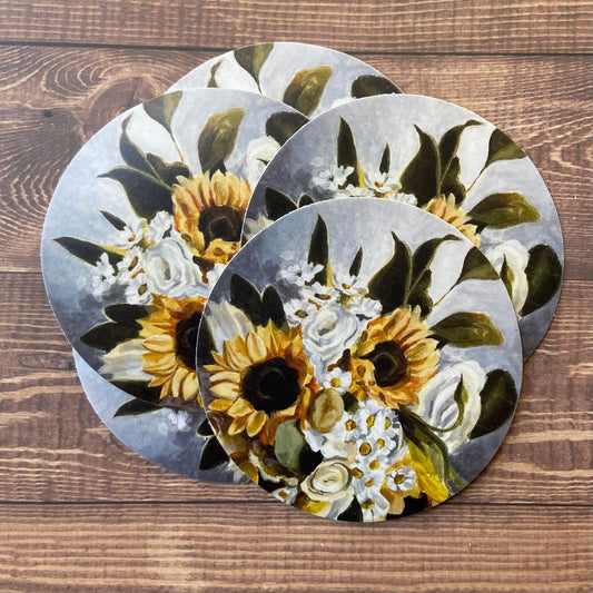 A small pile of round stickers of my painting "Green Gold", depicting a bouquet of sunflowers, daisies, white roses and greenery.