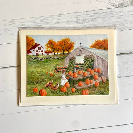 A folded cream-colored greeting card with an image of my painting, Homespun. Shown is a greenhousebuilding with dozens of pumpkins arranged outside. A little girl browses the gourds, accompanied by chickens. Farther away is a white farmhosue with a red roof, autumn orange trees, and a herd of resting cows. 