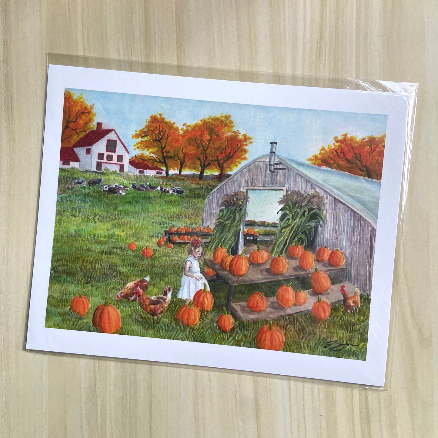 An art print of a fall-themed watercolor and gouache painting. The artwork depicts a little girl at a pumpkin patch with chickens. Across the grassy field, there is a farmhouse with trees in fall colors and cows resting. The print has a white border.