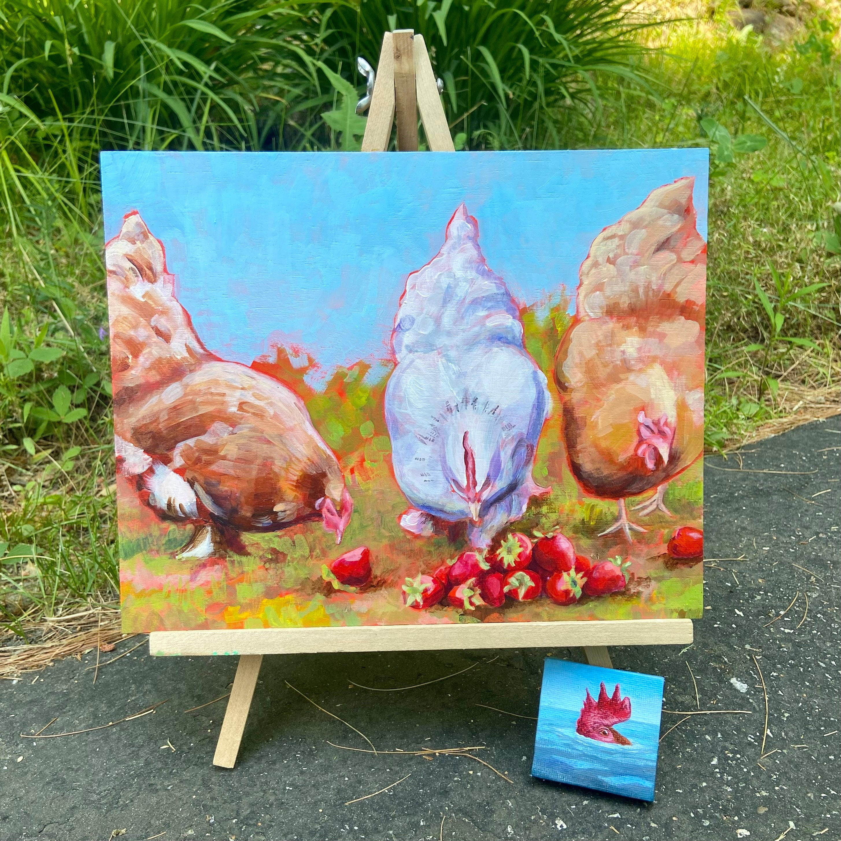 A staged image of my June 2024 painting Strawberry Hens on a tabletop easel outdoors, with smaller painting CAWS (ala Jaws) leaning in front of it.