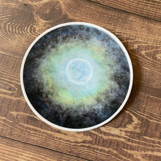 A round sticker showing a painting of the moon in a cloudy night sky. The clouds refract light to make a rainbow halo around the moon.