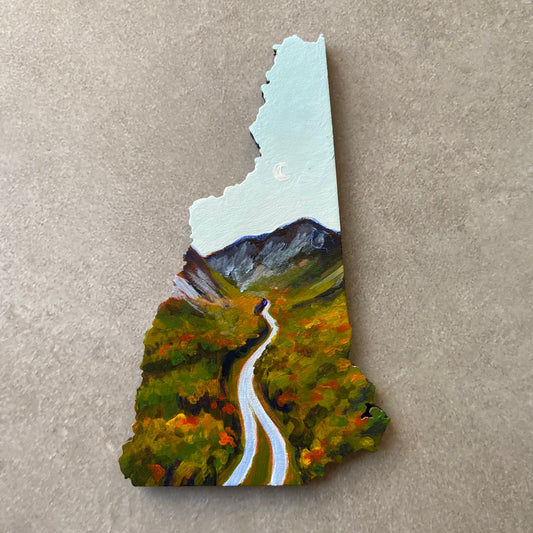 A New Hampshire-shaped painting of a highway extending into the distance towards mountains under a bright blue sky. It is the beginning of fall foliage season, with red and orange scattered in the forest, and there is a subtle crescent moon in the sky. 