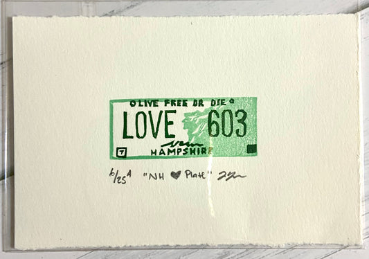 A miniature block print eraser print with the text 'LOVE 603' on a piece of paper, featuring green ink on a white background with a signature at the bottom.