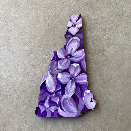 A New Hampshire-shaped painting depicting a close-up look at several blooming purple lilacs. 