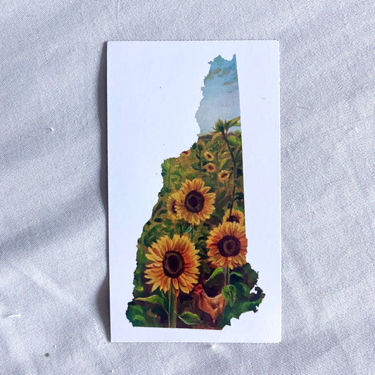 A rectangular magnet, white with a painting in the shape of New Hampshire in the middle. The painting shows a field of sunflowers, three pointed at the viewer, and an orange chicken at the bottom.