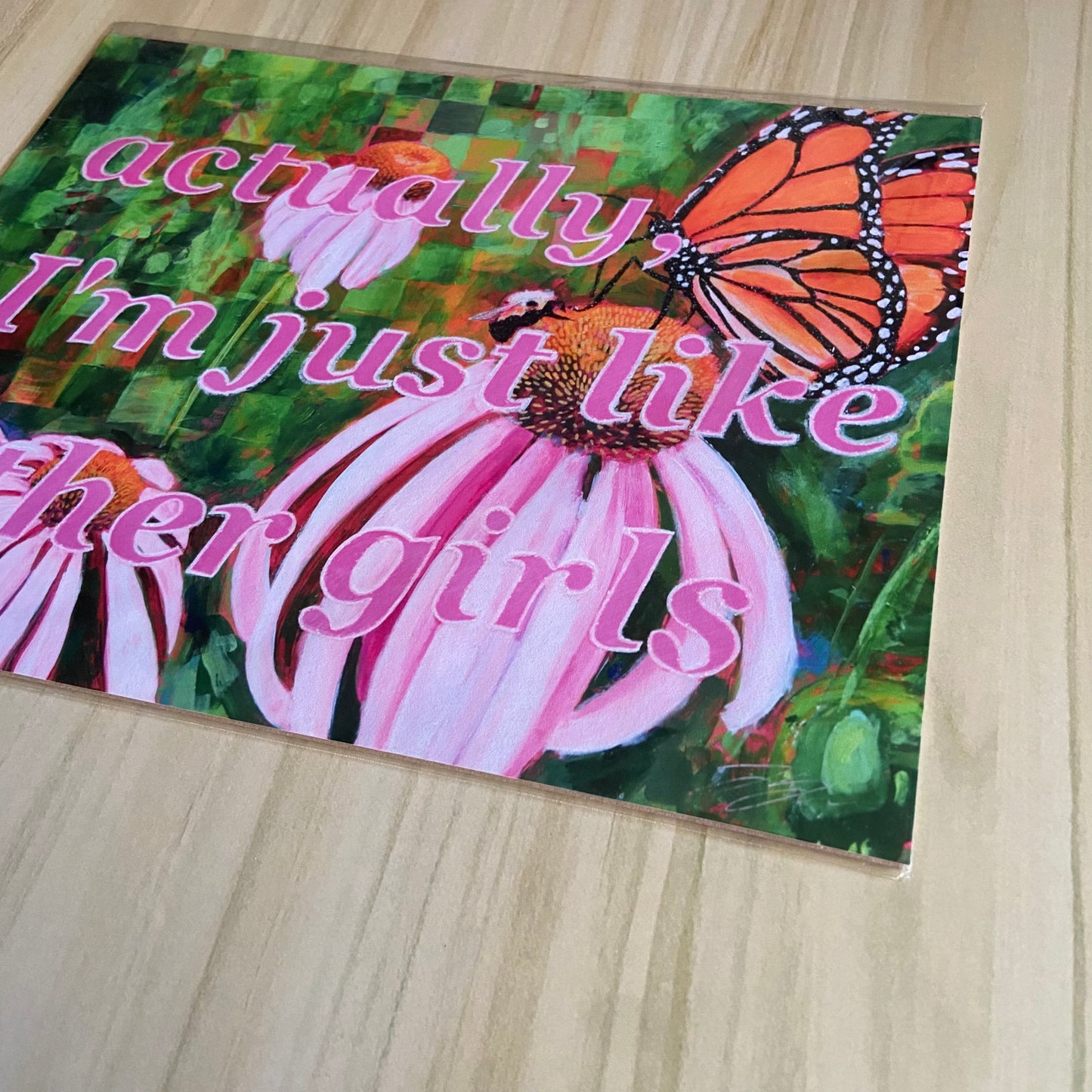 Detail view of the pink and green feminist art print. Pink text is shown over a garden background, depicting three flowers, a butterfly and bee. The painterly marks of the green abstract backdrop can be seen.