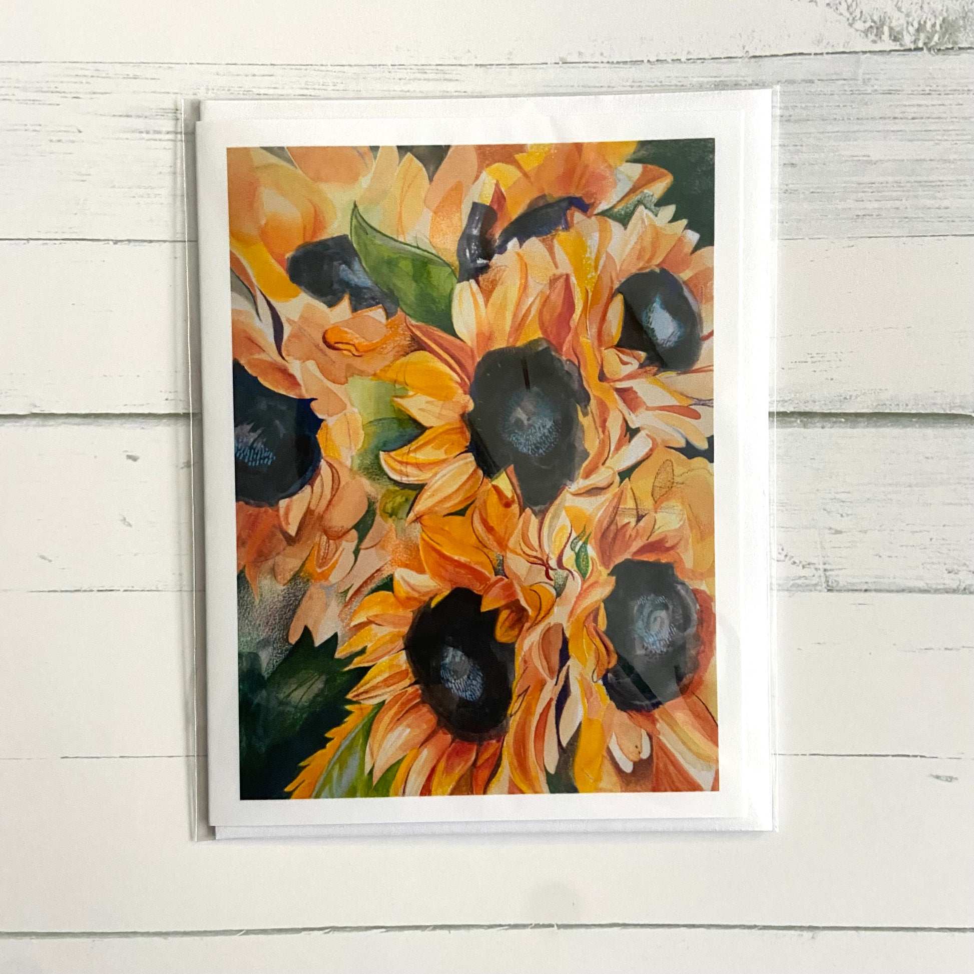 A folded white greeting card with a watercolor/mixed media painting on the front of several blooming sunflowers.