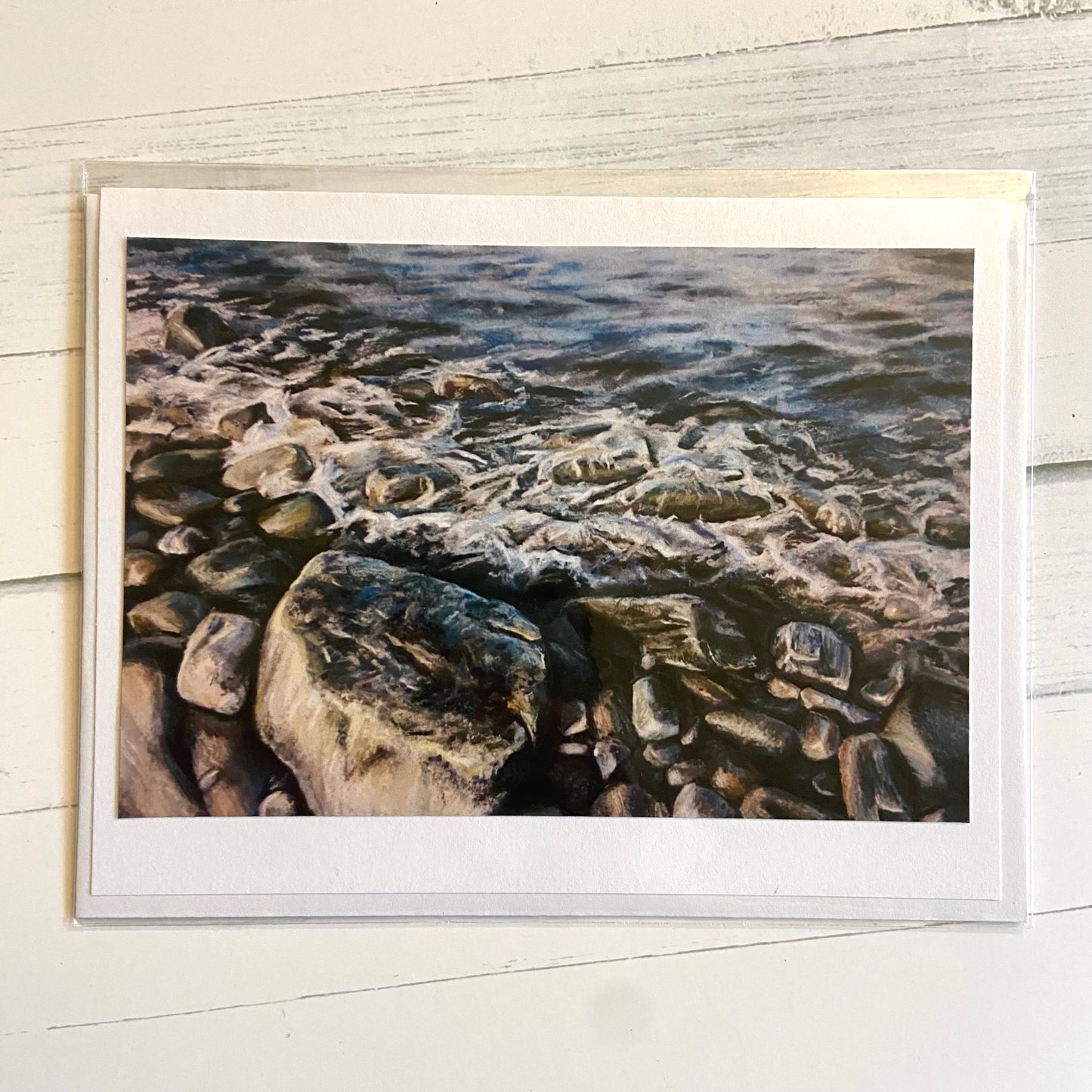 A folded white greeting card with an image of my painting, Quiet Moment. The pastel painting is a detailed view of waves meeting a rocky shore and all the interesting textures there.