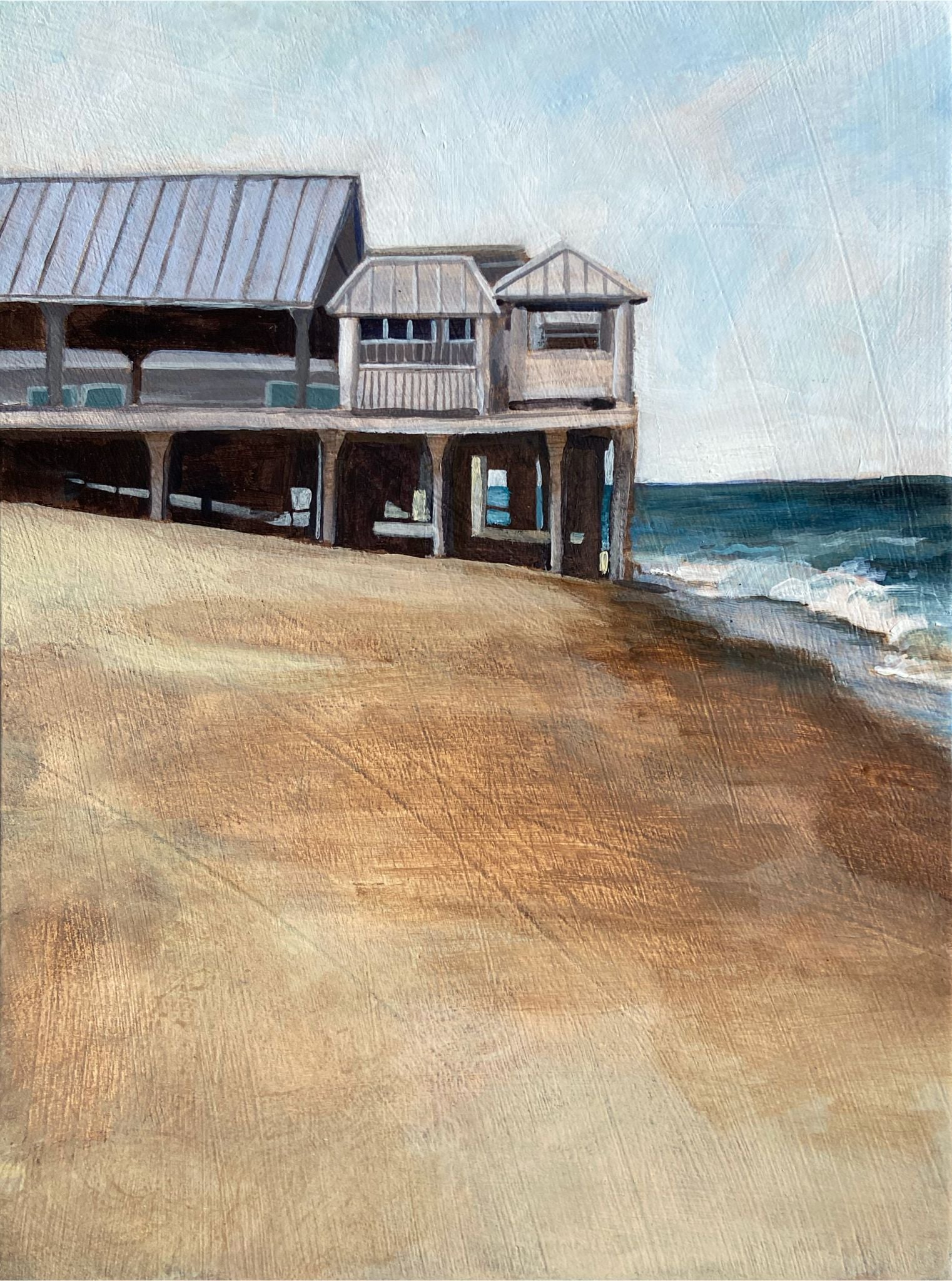 A vertically oriented landscape painting depicting some beachfront buildings on a tall pier, viewed from the sand. The pier comes from left to meet the ocean waves at right. The sky is pale blue and the sand is painterly in texture. 