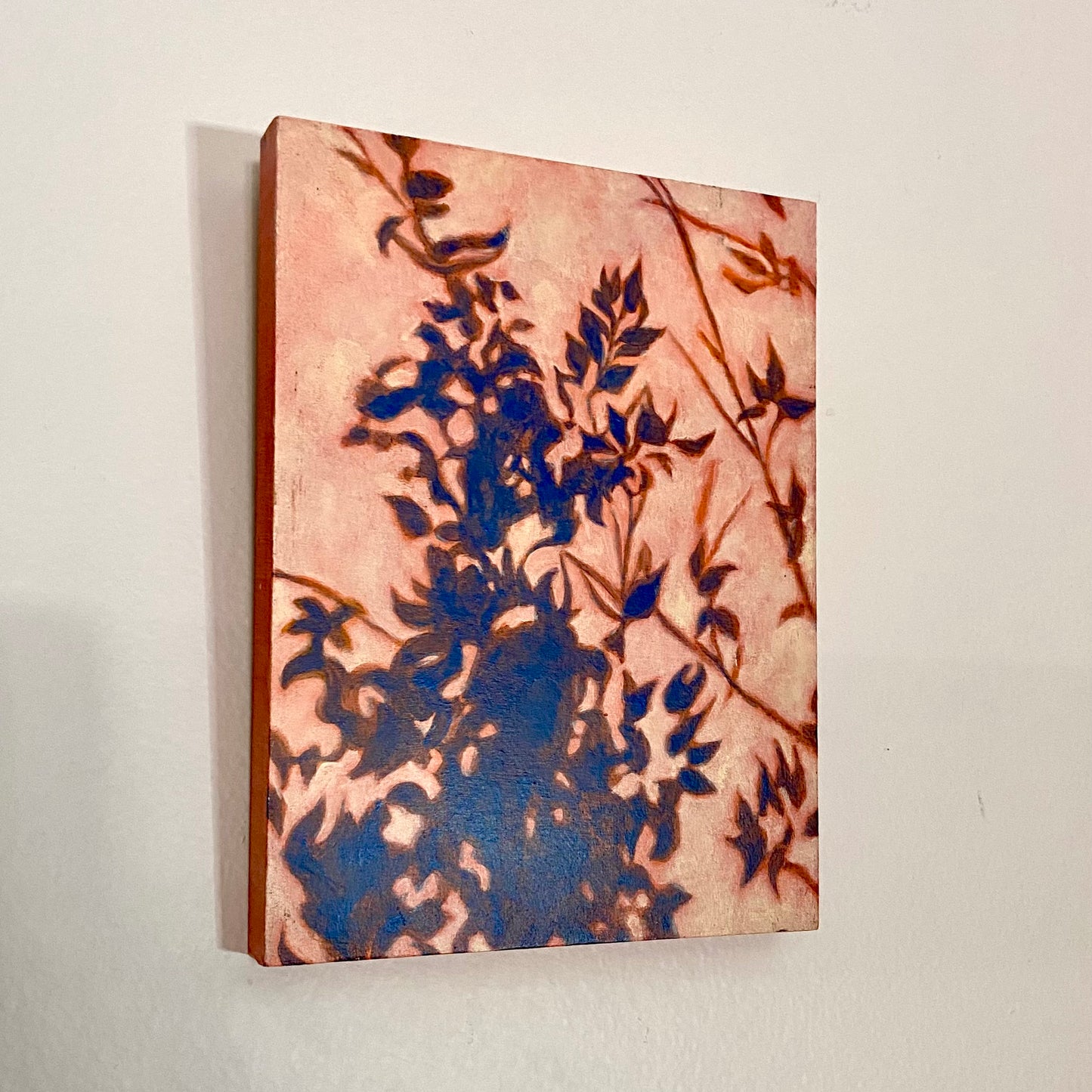 A vertical, rectangular painting of a plant's shadow. Blue shadows of leaves cover the picture plane in a natural pattern, more concentrated at the bottom and growing smaller toward the top. The negative space is pale yellow-orange. 