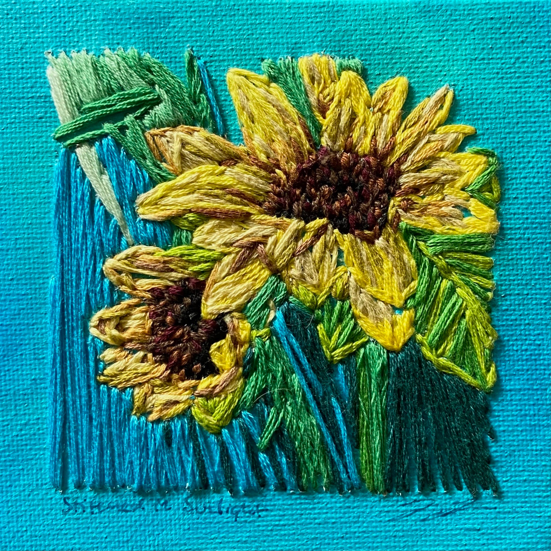 An embroidery on canvas piece of artwork, "Stitched in Sunlight", by artist Jackie Hanson. Two yellow sunflowers over a vibrant turquoise background.