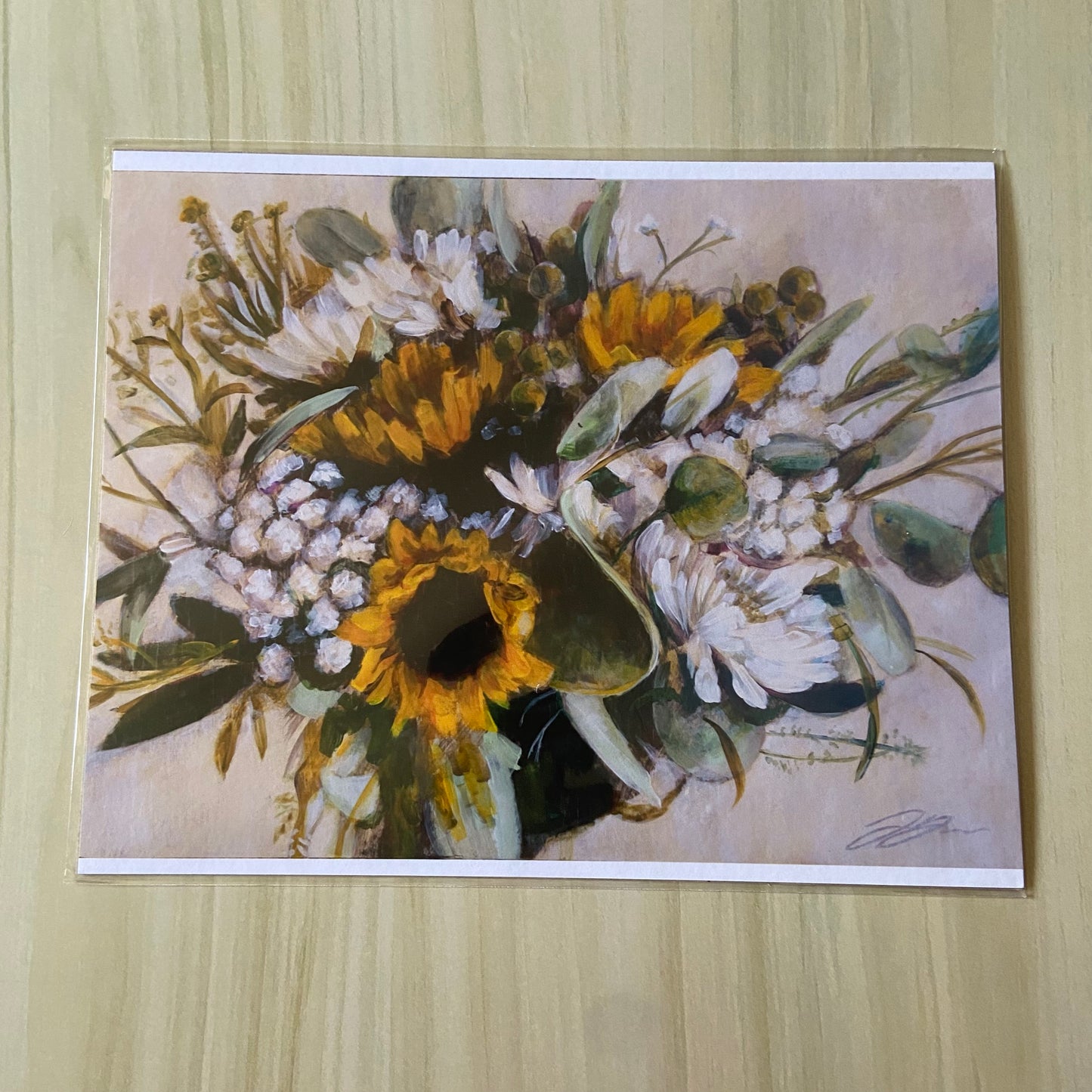 A print copy of a flower bouquet painting. The blooms are yellow sunflowers, assorted white flowers and greenery. The background is beige. Paint brush mark texture is visible in the petals, especially in the lightest floral parts. 